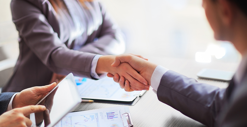 This image depicts a professional setting where two people are shaking hands across a table, likely indicating an agreement or a business deal.