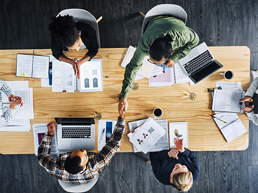 An overhead look of people sitting at a table with laptops and paper