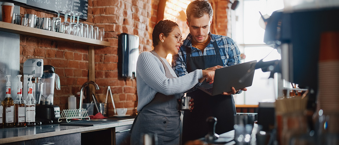 A man and woman looking at a laptop in a restaurant